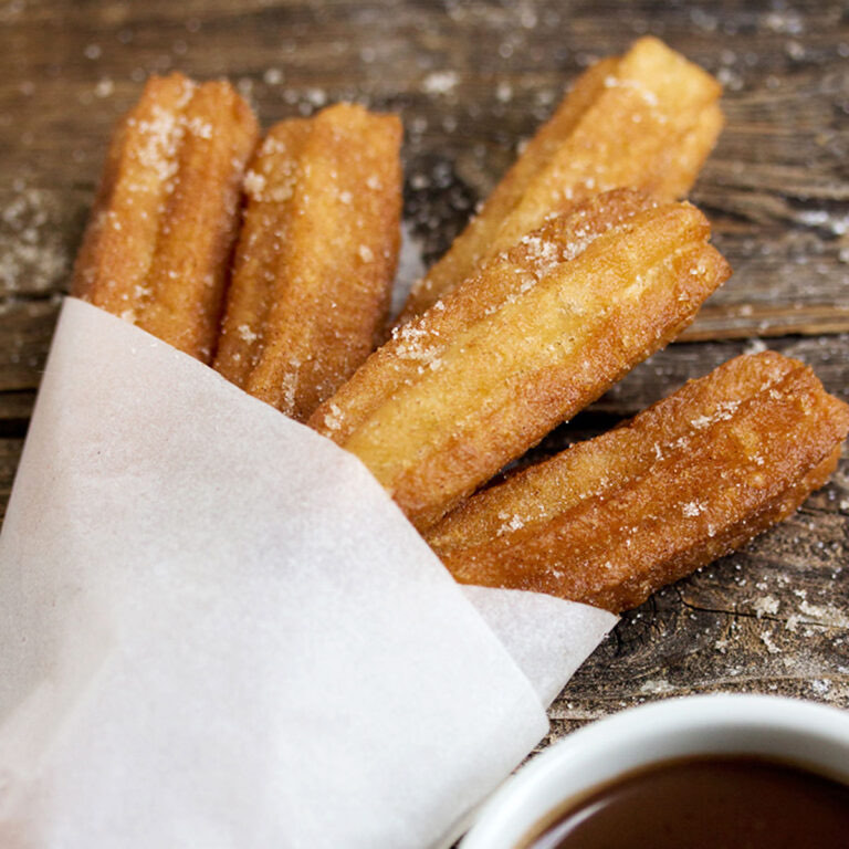 Čerstvě usmažené churros posypané cukrem v papírovém kornoutu