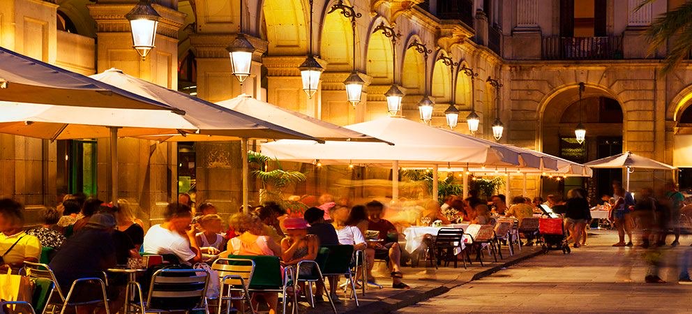 Noční restaurační terasa s bílými slunečníky na náměstí v Barceloně
