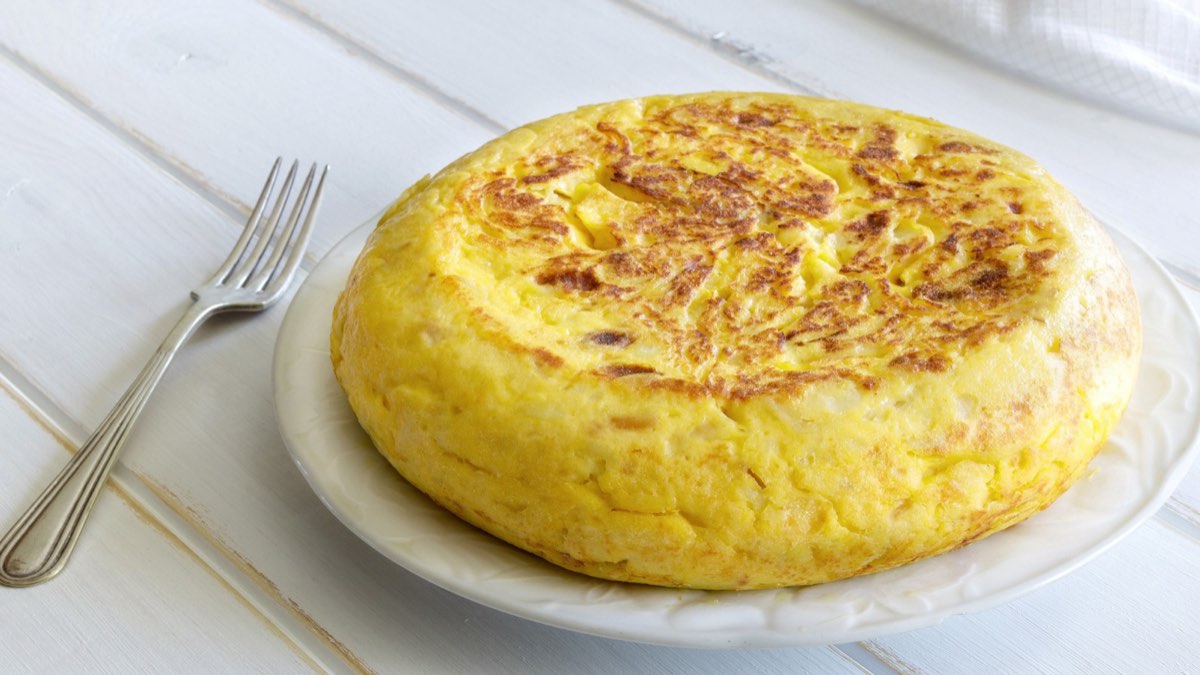 Celá vysoká tortilla de patatas na talíři s vidličkou