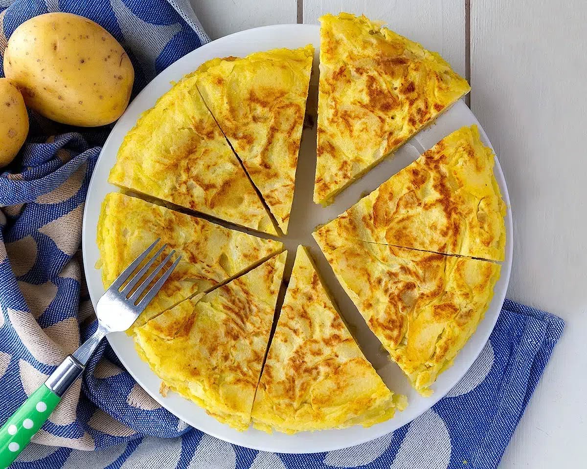 Tortilla de patatas nakrájená na trojúhelníky, vedle syrové brambory