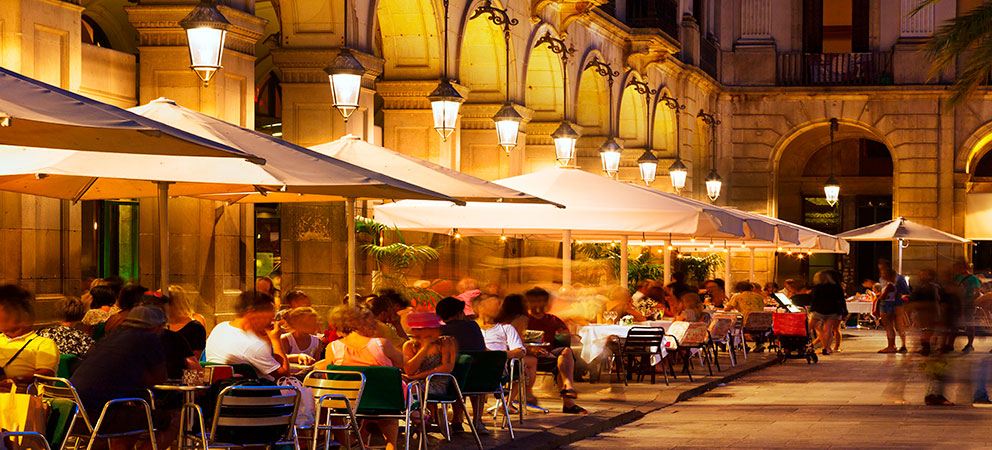 Noční restaurační terasa s bílými slunečníky na náměstí v Barceloně